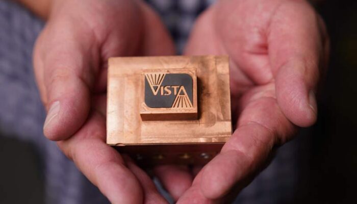A close-up photo of hands cradling a metal lighting component that features the Vista logo